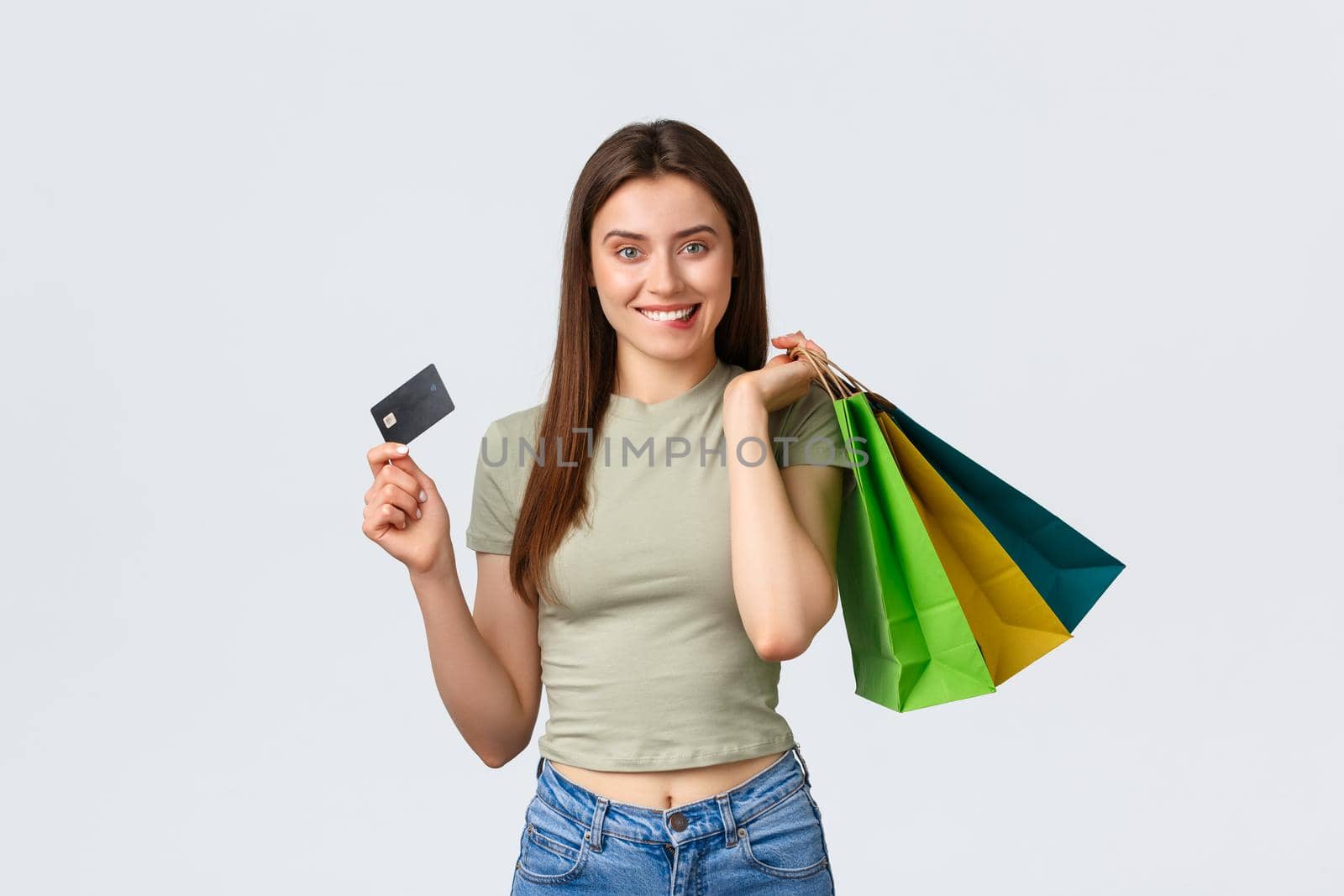 Shopping mall, lifestyle and fashion concept. Excited smiling young woman biting lip, tempt to waste all money on credit card, holding bags with clothes and looking pleased, white background.