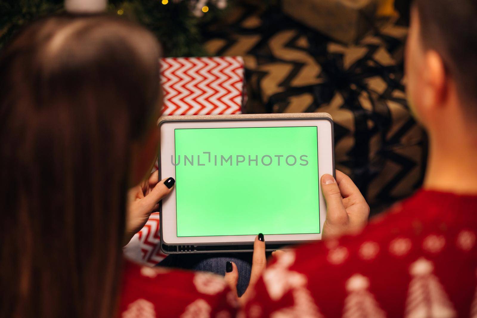 Hands holding a tablet computer with green mock up screen. Caucasian couple using tablet for christmas video call with happy couple on screen. Christmas, festivity and communication technology.
