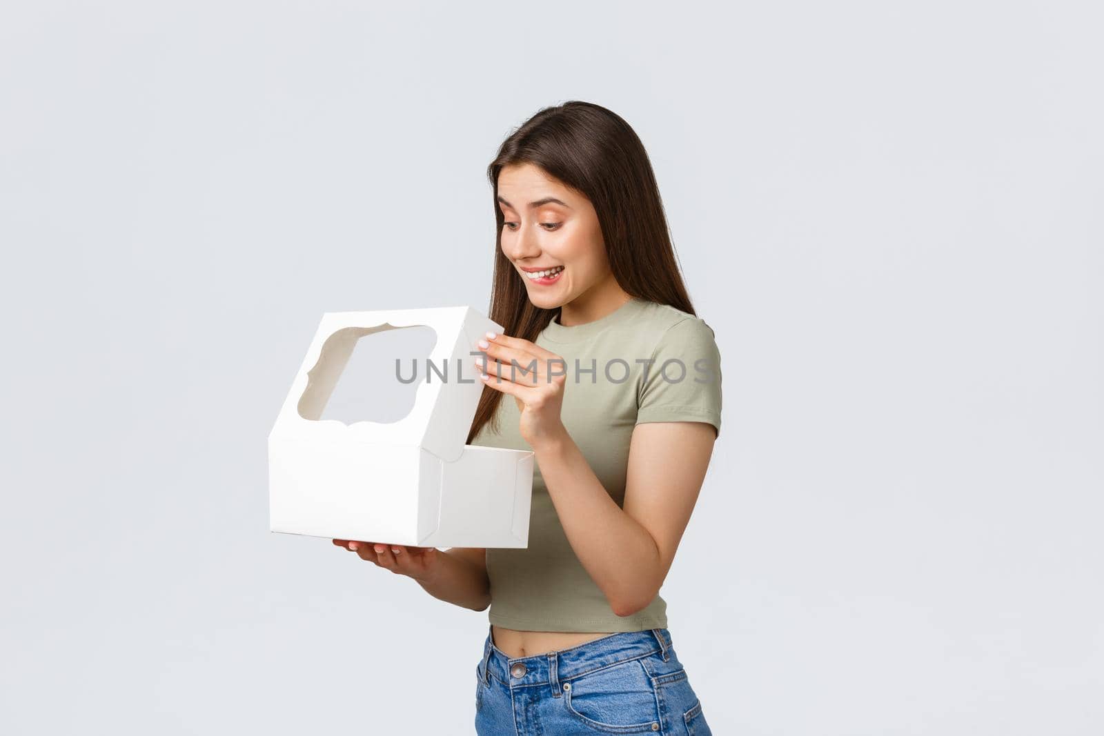 Delivery, lifestyle and food concept. Smiling happy girlfriend open white box with sweet delicious desserts, cake or muffins ordered in best pastry shop, standing white background.