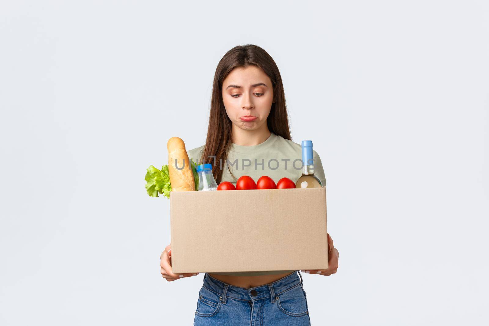 Online home delivery, internet orders and grocery shopping concept. Disappointed female customer receive wrong order of groceries, looking upset inside box and pouting, stand white background.