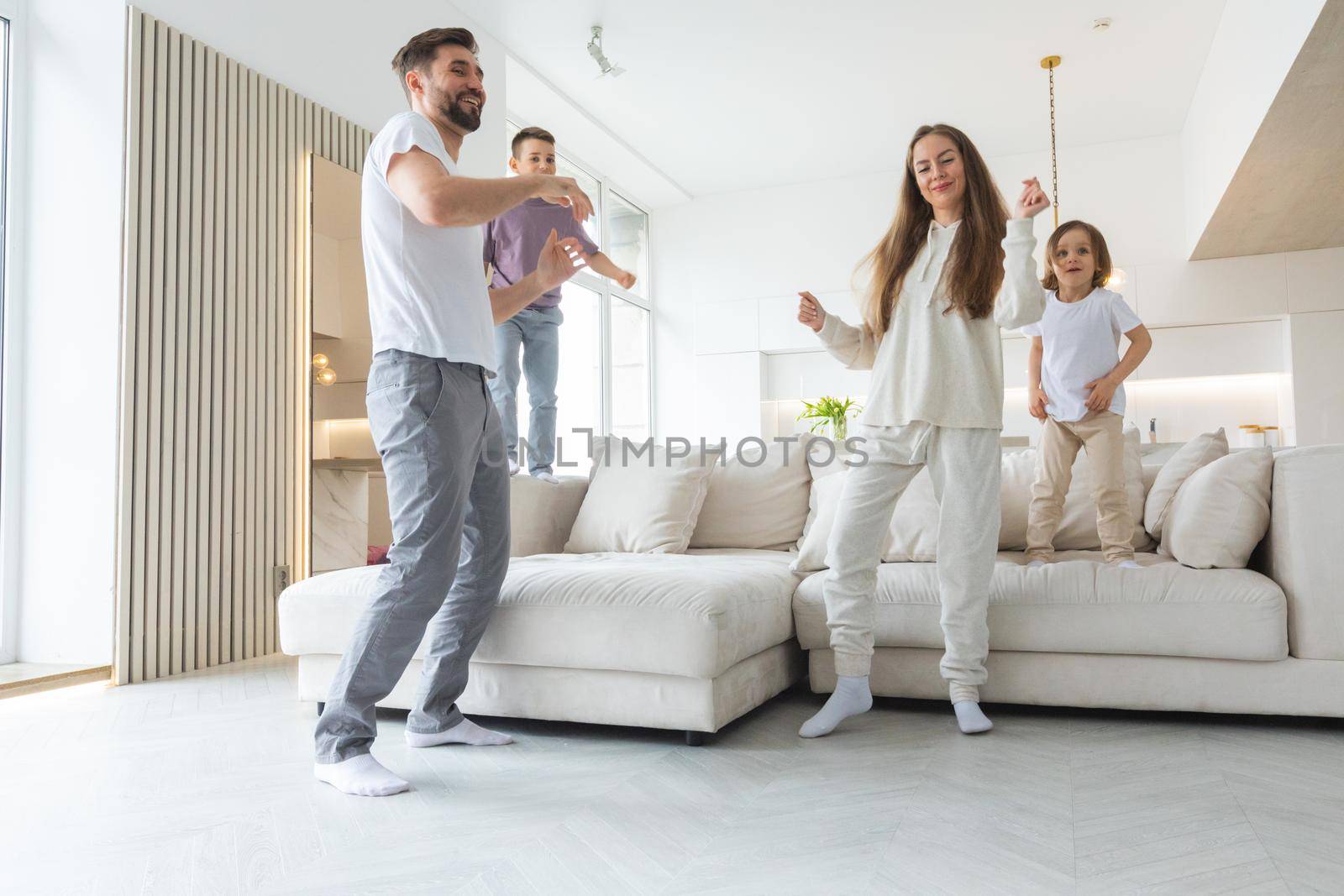 Family having fun at home. Married couple with little kids dancing moving in living room. Happy family spend time together concept