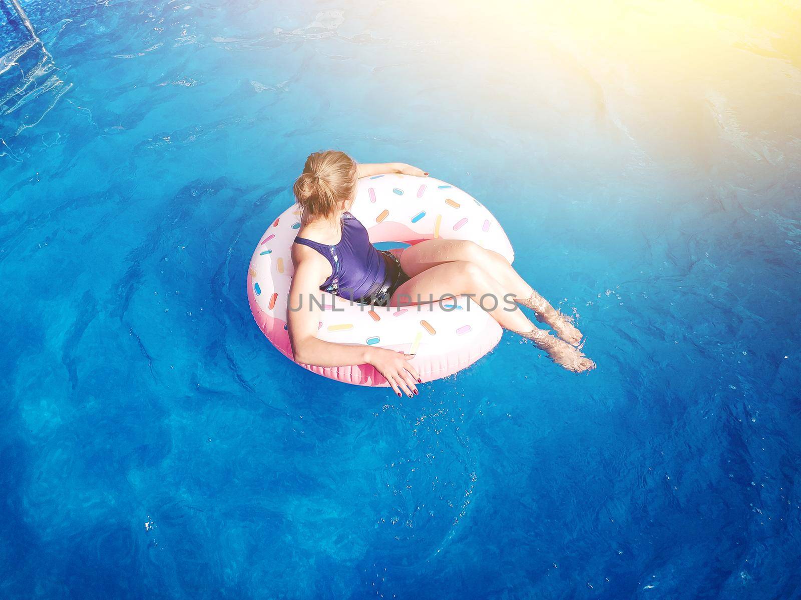 Summer warm vacation.The girl sits on a rubber ring in the form of donut in blue pool in the sun.Time to relax on an air mattress. Having fun in the water for a family vacation.Sea resort.Copy space.