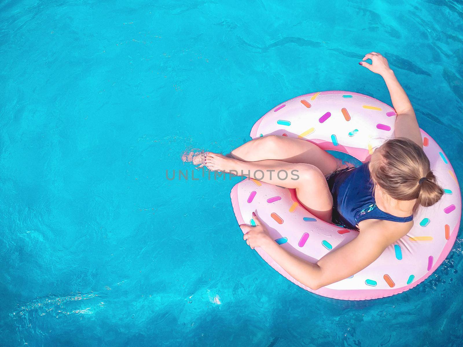 Summer warm vacation. The girl sits on a rubber ring in the form of a donut in a blue pool. Time to relax on an air mattress. Having fun in the water for a family vacation. Sea resort. Copy space.