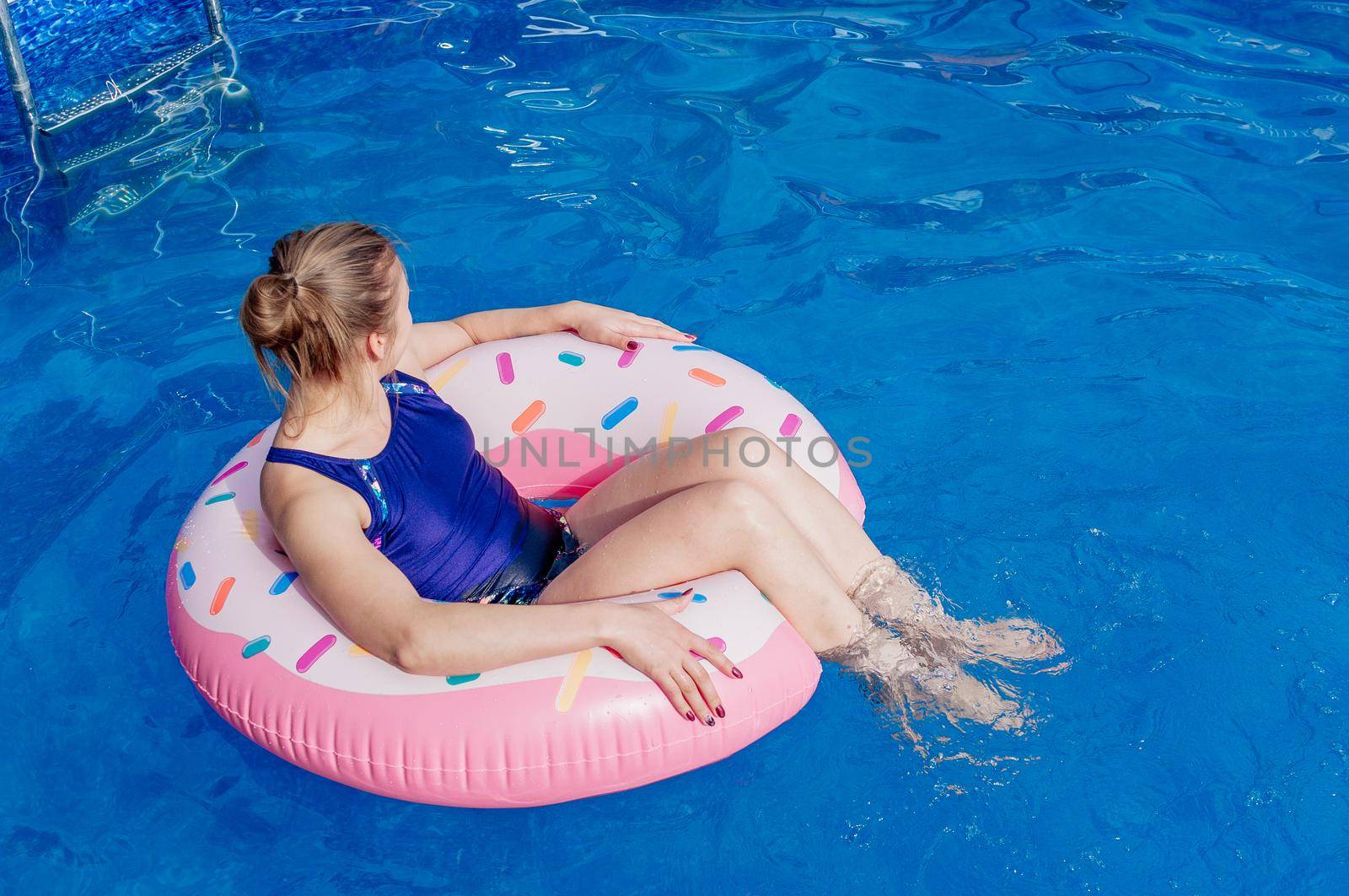 Summer warm vacation. The girl sits on a rubber ring in the form of a donut in a blue pool. Time to relax on an air mattress. Having fun in the water for a family vacation. Sea resort. Copy space. by Alla_Morozova93