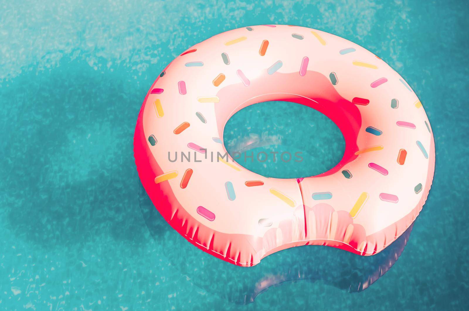 An inflatable pink donut with white icing floats in a blue pool. An inflatable circle for swimming on water in the warm season. The concept of summer spending time. Beach summer composition