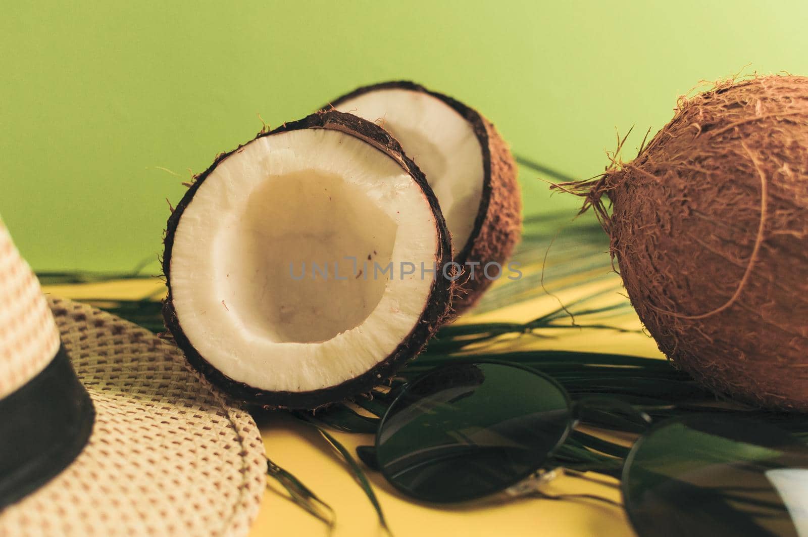 Summer composition. Tropical palm leaves, hat, glasses and broken coconut on a sandy background. The concept of the summer season, parties and heat. Side view