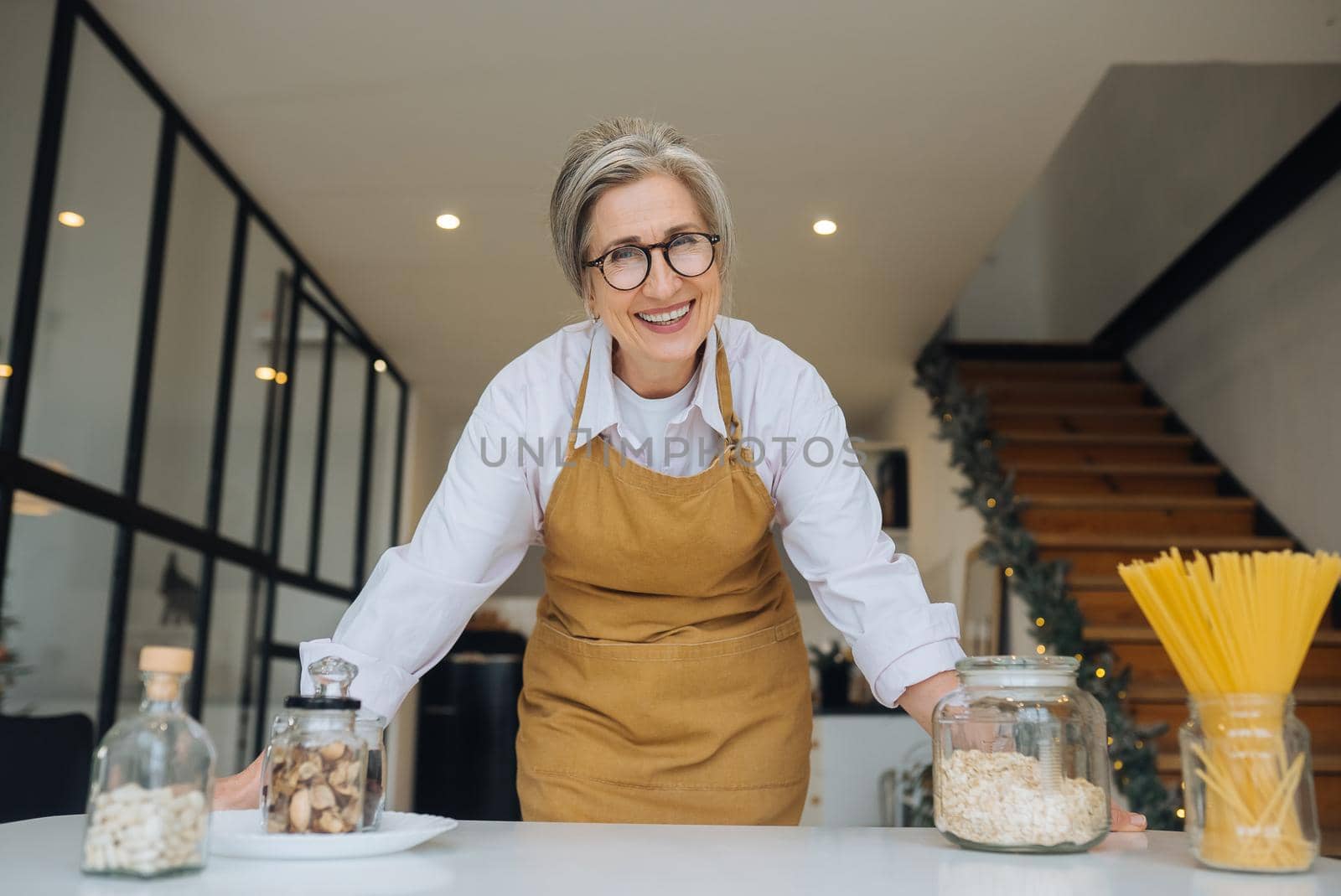 Smiling middle aged mature grey haired woman looking at camera, happy old lady in glasses posing at home indoor