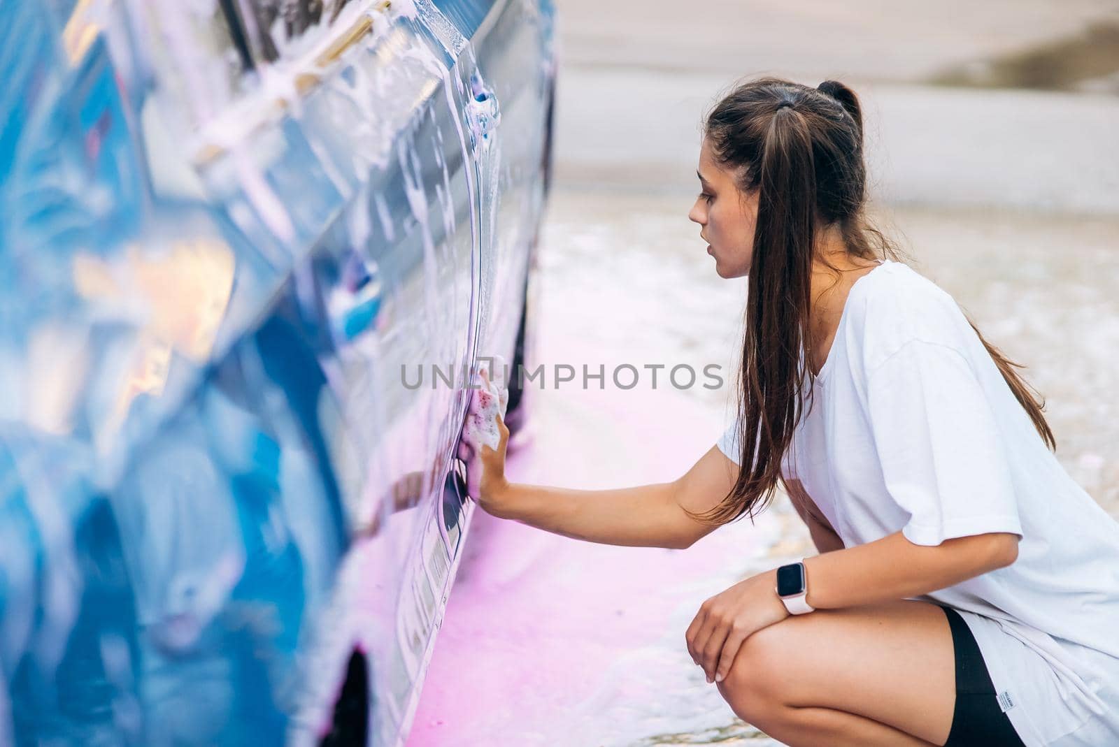 Woman with two pigtails with a sponge washes the side of the car