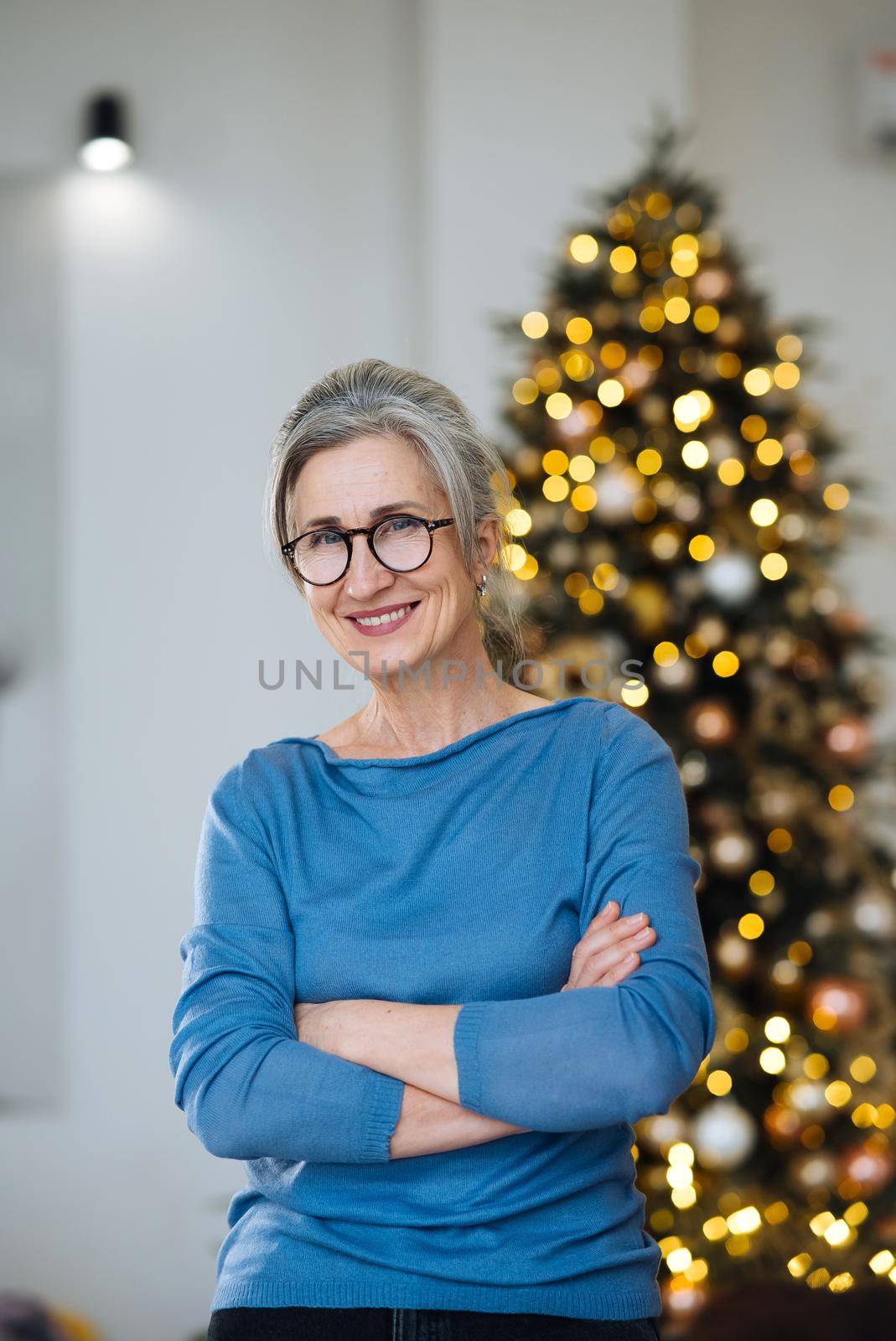 Elderly lady smiling and looking in camera, Xmas tree sparkling on background