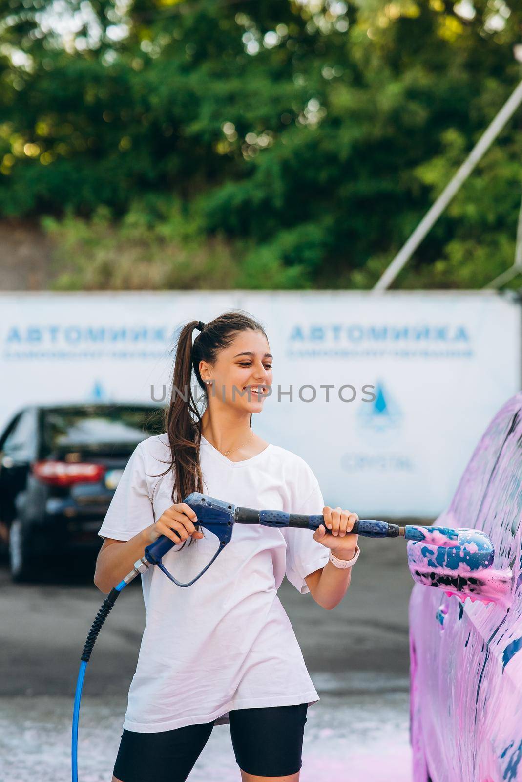 Woman with high pressure hose stands by car