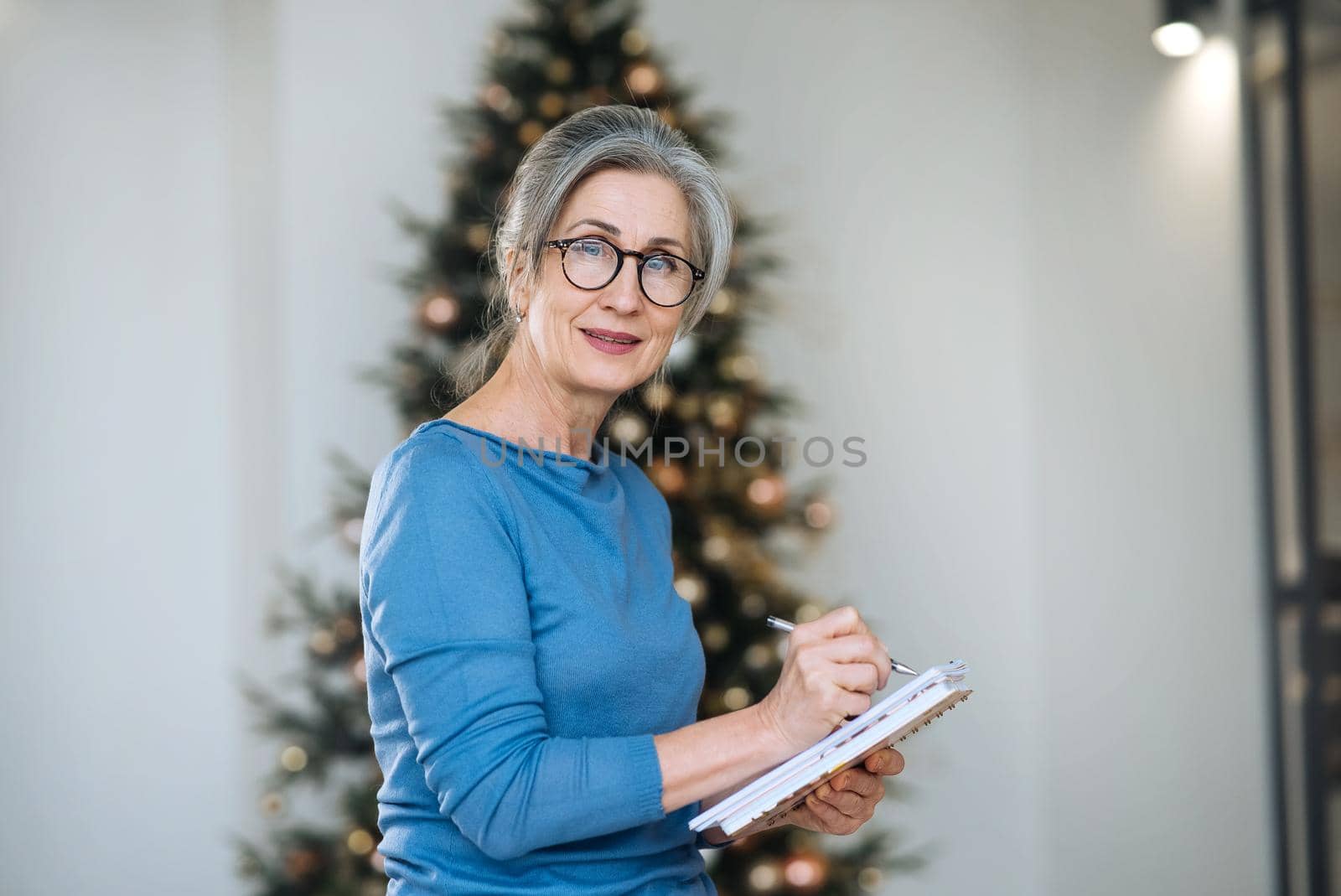 Happy senior woman in glasses writing to notebook or diary at home