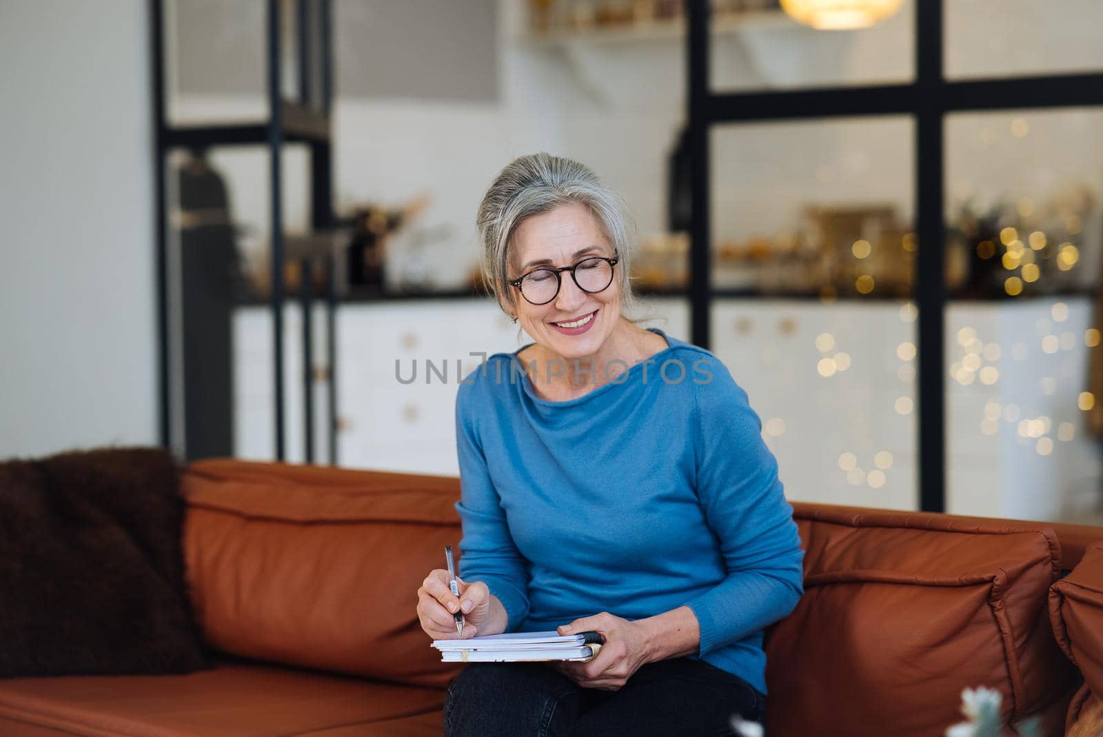 Happy senior woman in glasses writing to notebook or diary at home