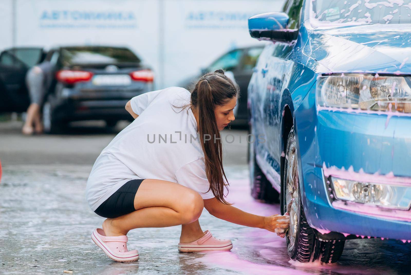 Brunette with two pigtails with a sponge washes the rim of a car