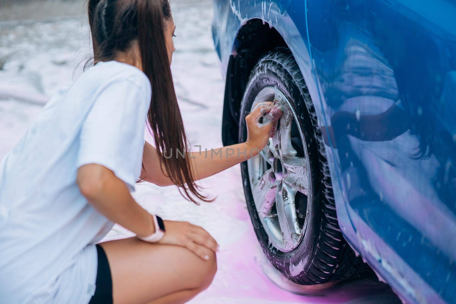 Brunette with two pigtails with a sponge washes the rim of a car