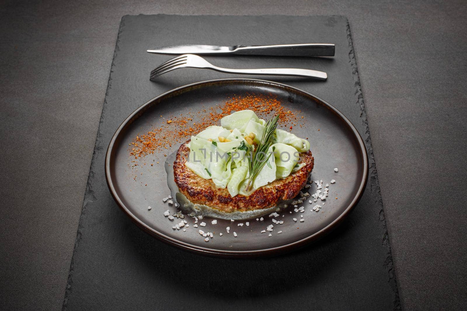 Roasted cutlet from beef and pork meat with zucchini slices and pine nuts. Black background. Front view