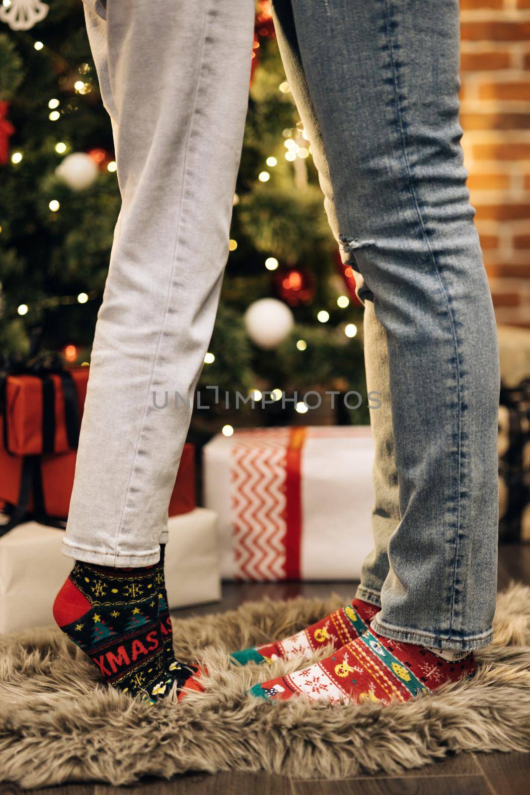 Two pairs of foot, dressed in Xmas soks. Atmosphere of Christmas. Legs in winter christmas socks in cozy home interior. Christmas socks. The idea for happy family. Feet in colorful wool socks.