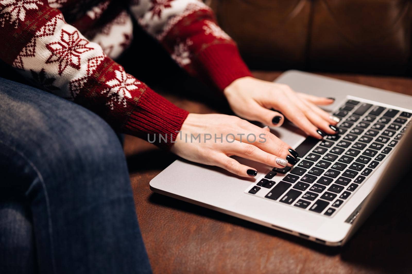 Hands working on laptop with christmas ornaments. Girl using laptop sitting on the sofa by christmas tree. Freelance and remote work during holidays. Christmas online store. Xmas shop. Christmas sales