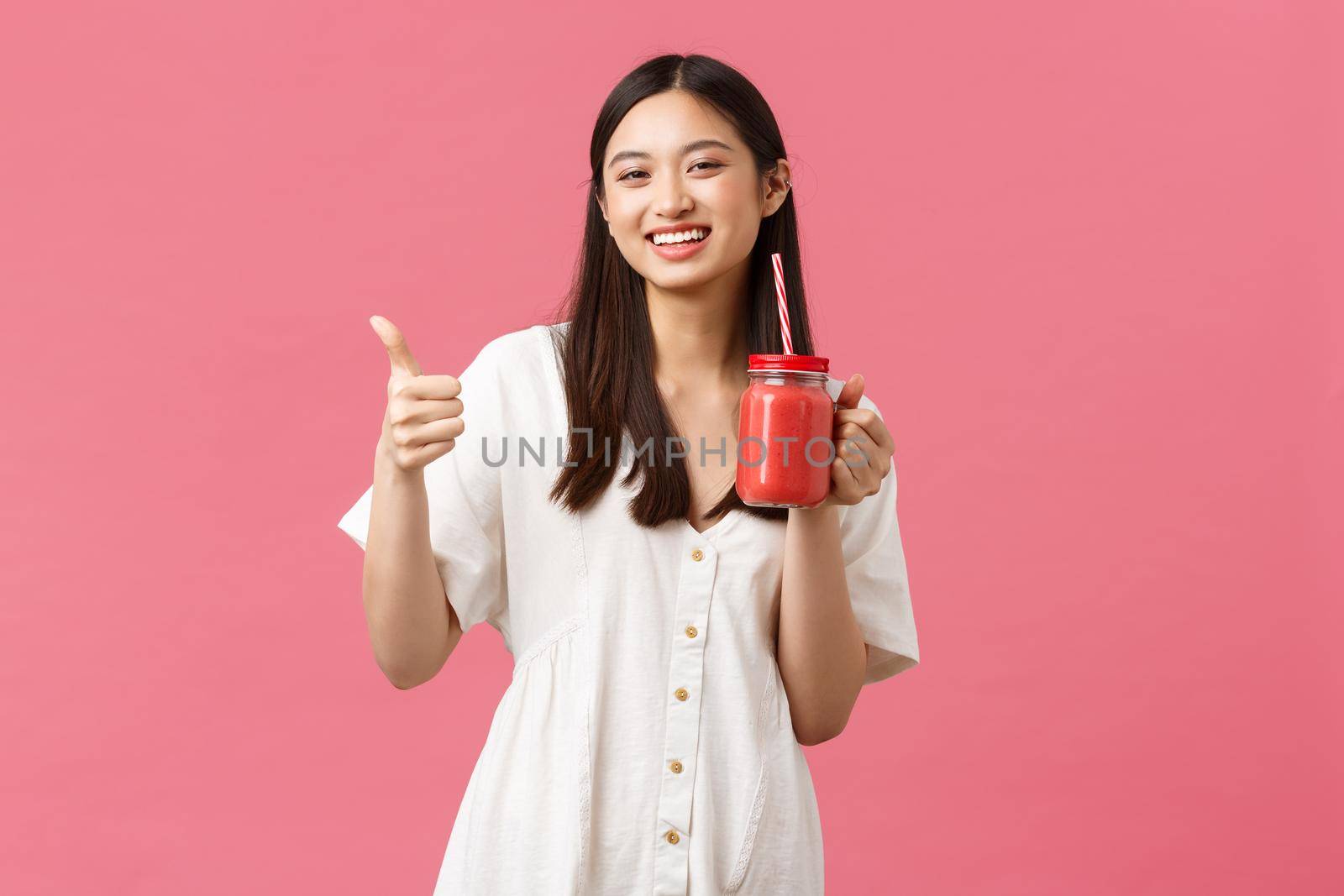 Healthy food, emotions and summer lifestyle concept. Upbeat happy, satisfied female cafe visitor enjoying delicious smoothie, showing thumbs-up as recommend drink, pink background.