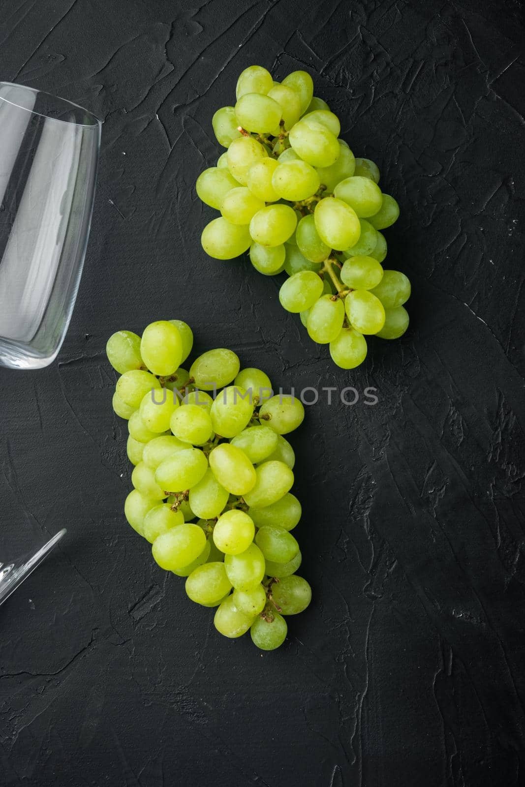 Wineglasses with grapes set, on black stone background, top view flat lay