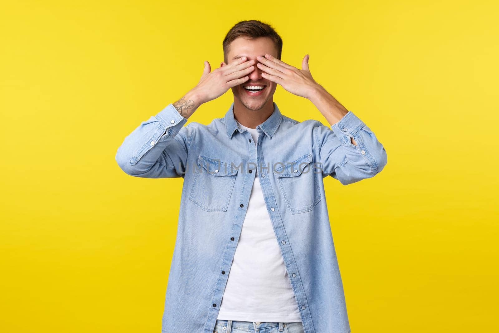 Lifestyle, people emotions and summer leisure concept. Smiling happy handsome man shut eyes with hands and anticipating for surprise, standing upbeat at birthday party, yellow background by Benzoix