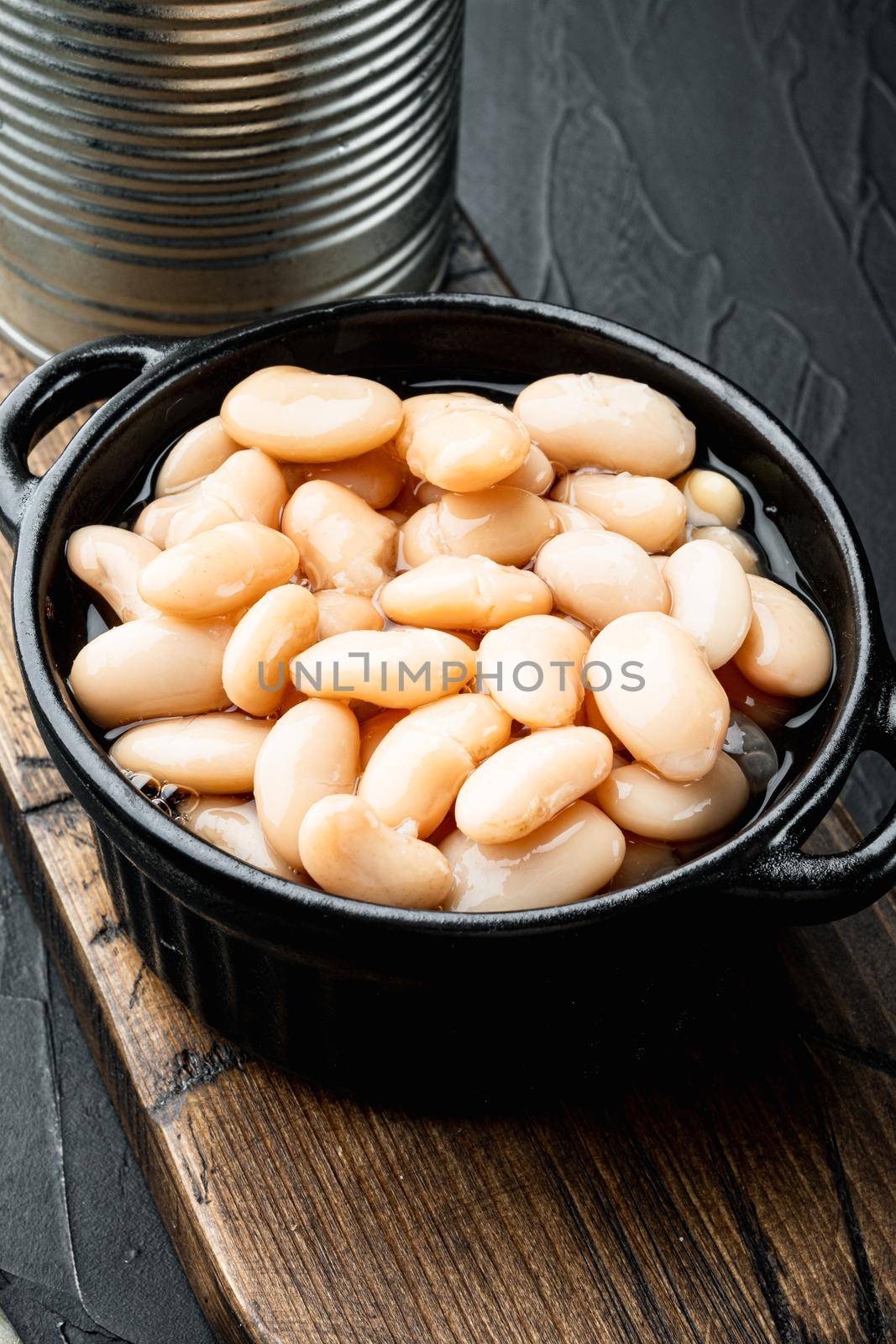 Canned white beans set, with metal can, in bowl, on black stone background