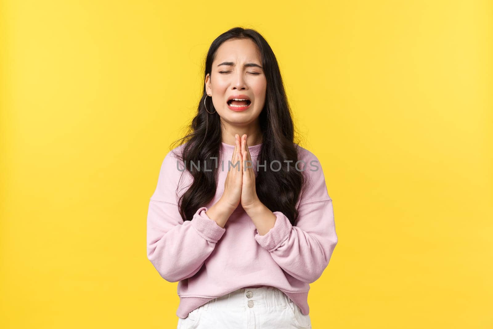 People emotions, lifestyle and fashion concept. Desperate and sad gloomy asian girl begging for forgiveness, crying heart out and praying, pleading god mercy, standing yellow background.
