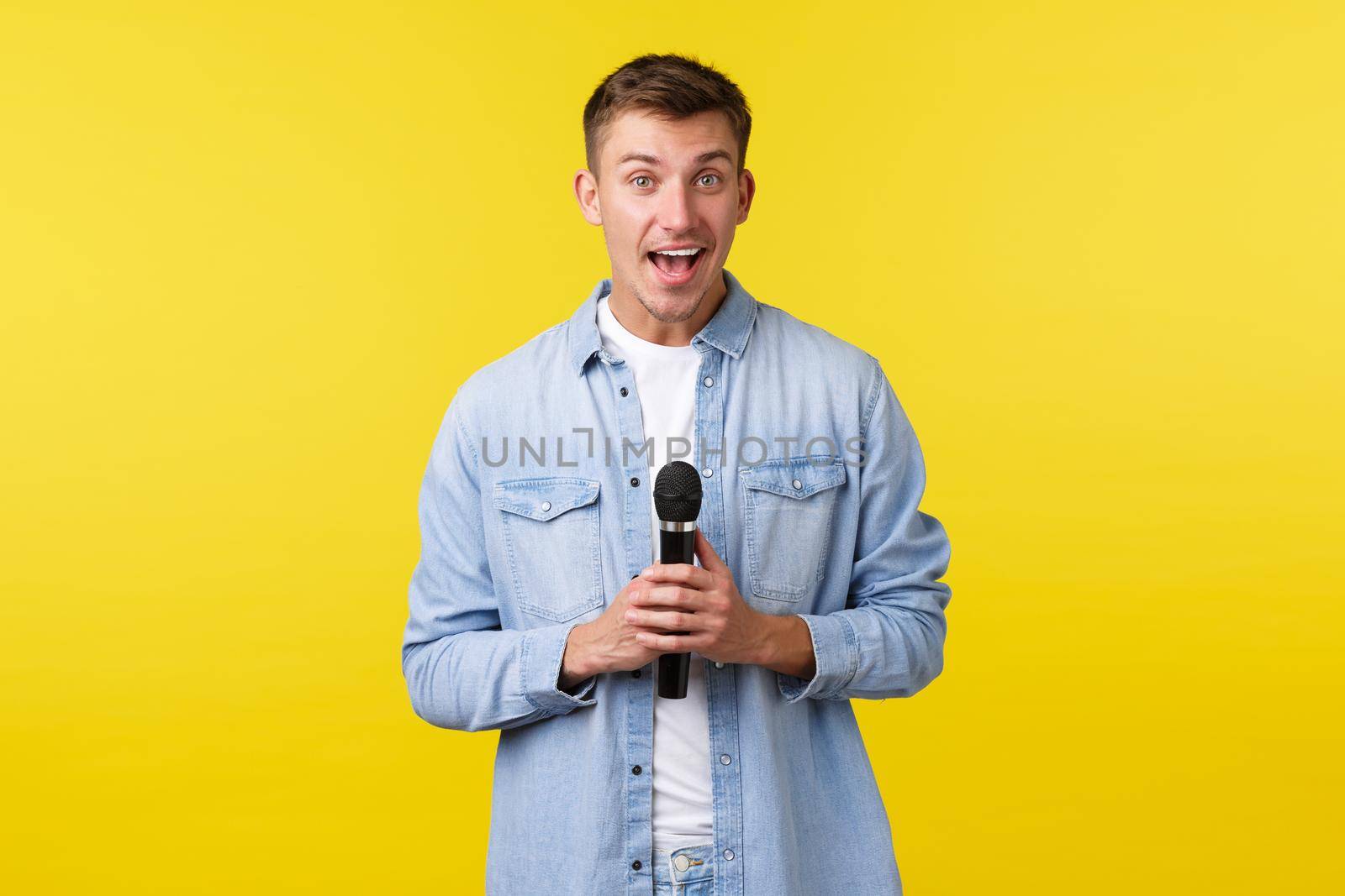 Lifestyle, people emotions and summer leisure concept. Lively happy handsome blond man looking away and smiling, talking on stage, perform stand-up or singing karaoke with microphone by Benzoix