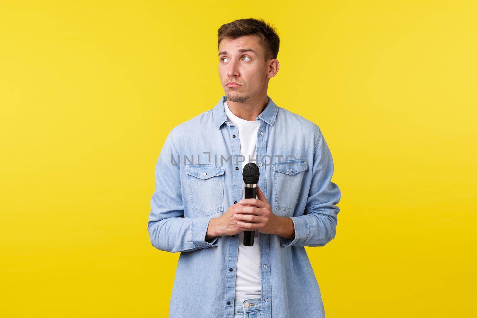 Lifestyle, people emotions and summer leisure concept. Thoughtful dreamy handsome man looking away, thinking as holding microphone, standing yellow background indecisive.