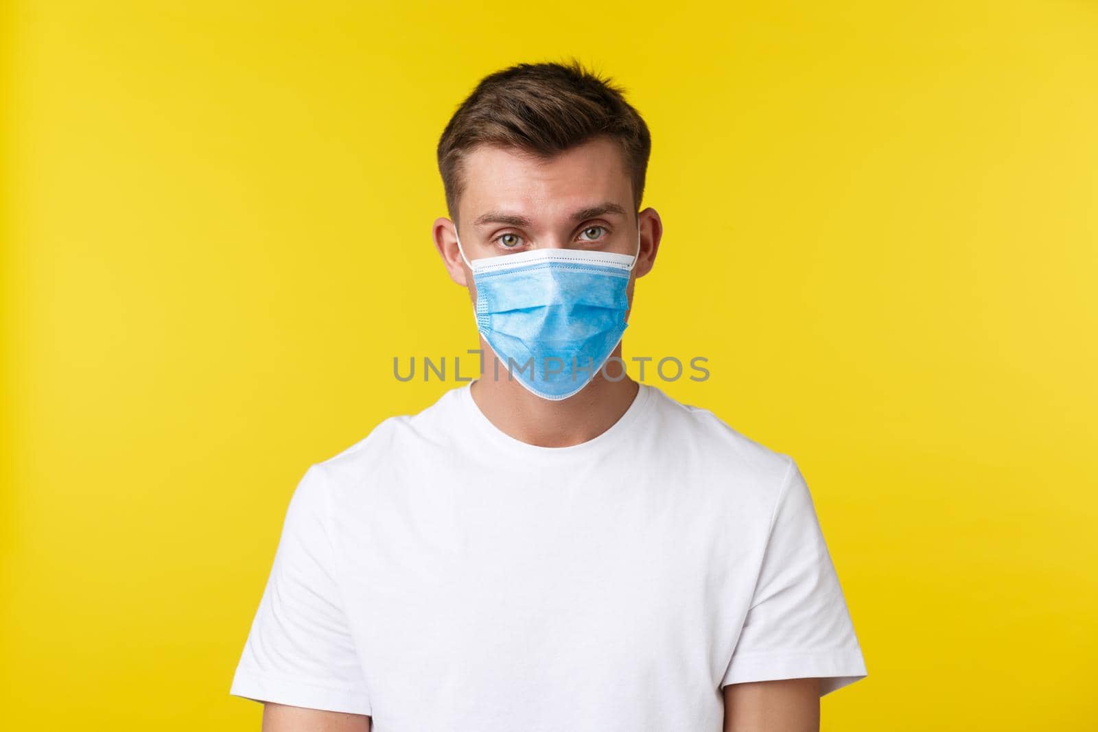 Concept of social distancing, covid-19 and people emotions. Serious man in medical mask and basic t-shirt looking at camera concerned, self-isolate himself from people and work from home by Benzoix