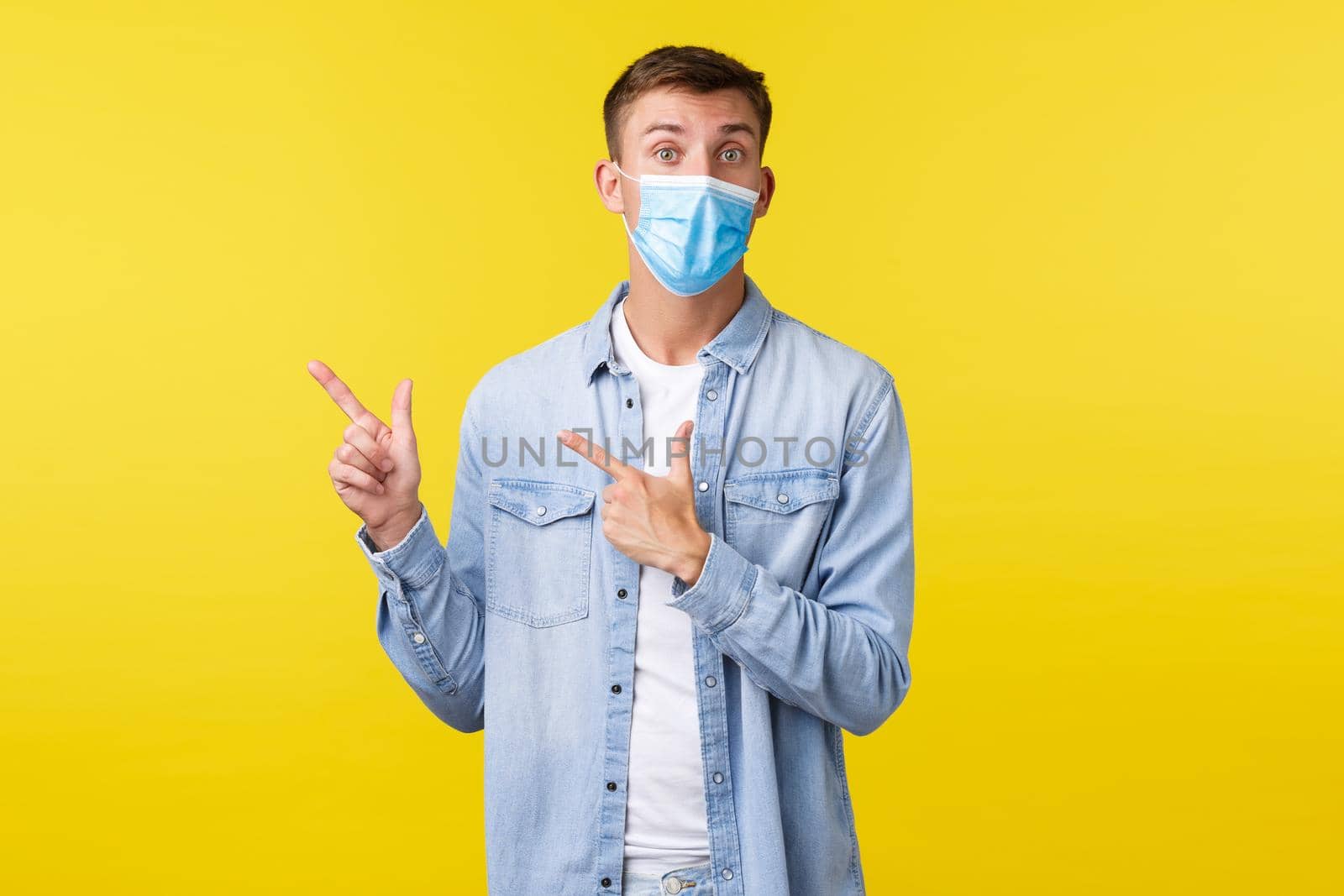 Concept of covid-19 pandemic outbreak, lifestyle during coronavirus social distancing. Excited handsome man in medical mask provide information on quarantine, pointing upper left corner.