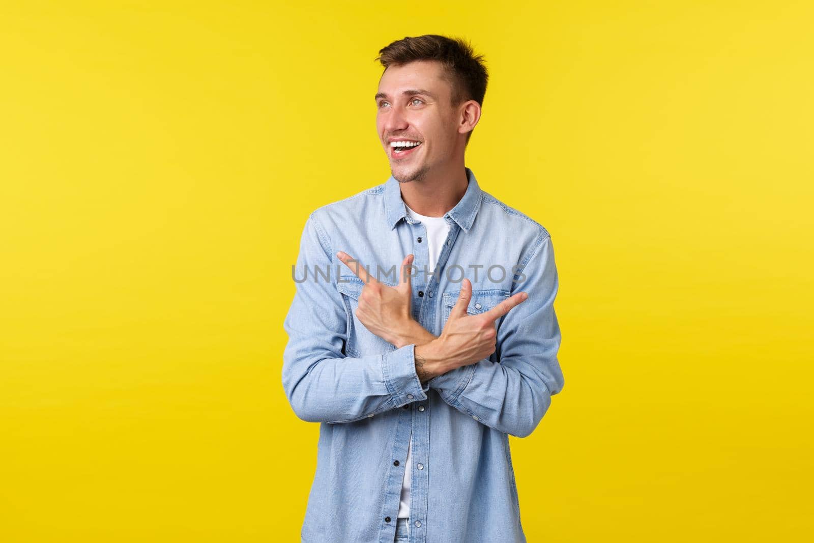 Portrait of handsome smiling blond man in casual clothes laughing and looking left while pointing sideways. Cheerful male customer shopping in store, make choice between two variants.