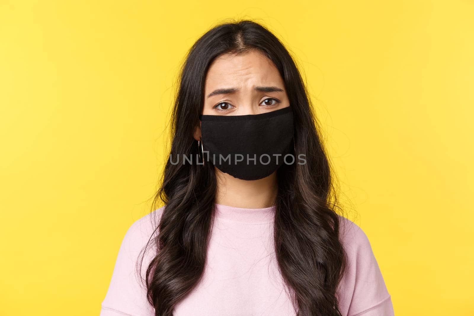 Covid-19, social-distancing lifestyle, prevent virus spread concept. Pity and sad asian gloomy girl frowning, wear face mask, feeling compassion and sadness, standing yellow background by Benzoix