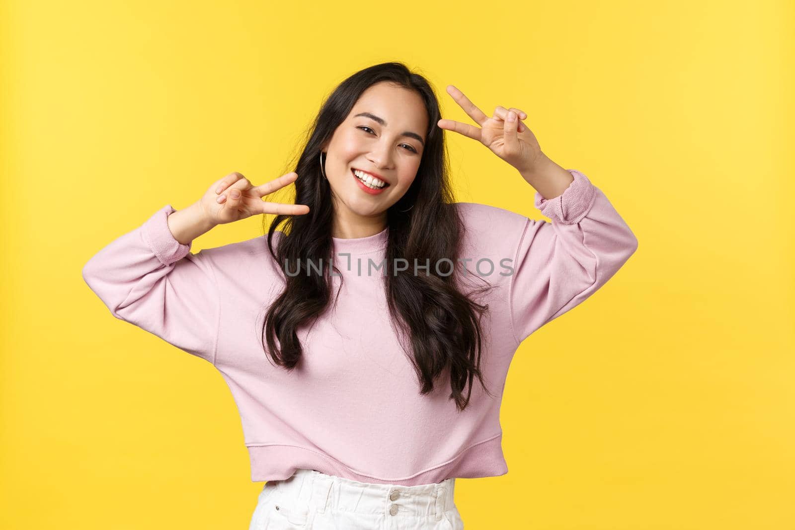 People emotions, lifestyle leisure and beauty concept. Cheerful and optimistic asian girl in stylish clothes, showing peace signs and smiling broadly, enjoying summer, yellow background by Benzoix