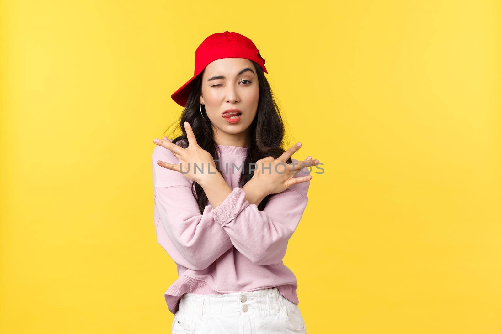 People emotions, lifestyle leisure and beauty concept. Cool and sassy stylish asian girl in red hip hop cap, showing swag gesture and smirk daring, standing confident over yellow background.