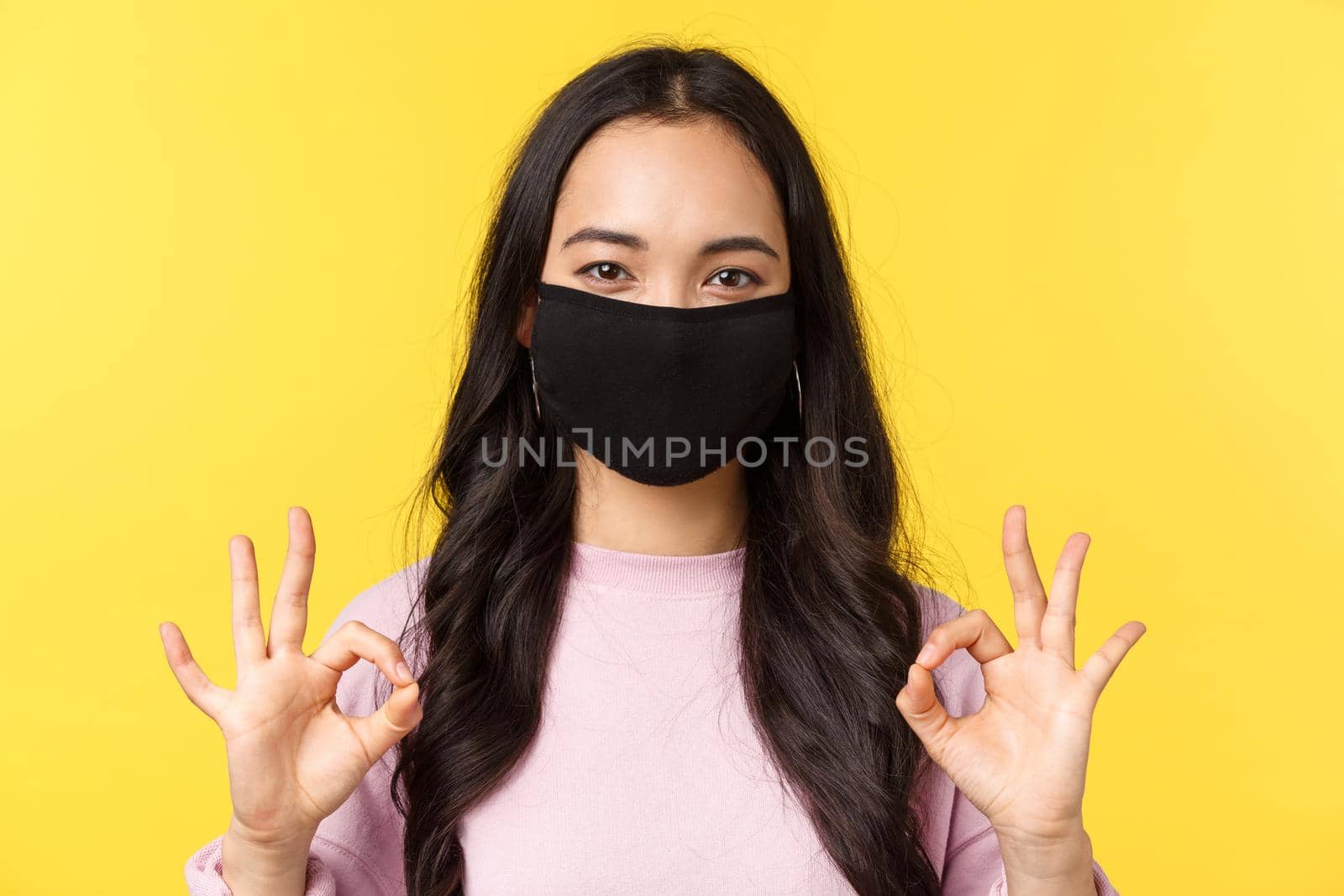 Covid-19, social-distancing lifestyle, prevent virus spread concept. Close-up of happy smiling asian female in face mask, take all under control, showing okay sign in like and recommend by Benzoix