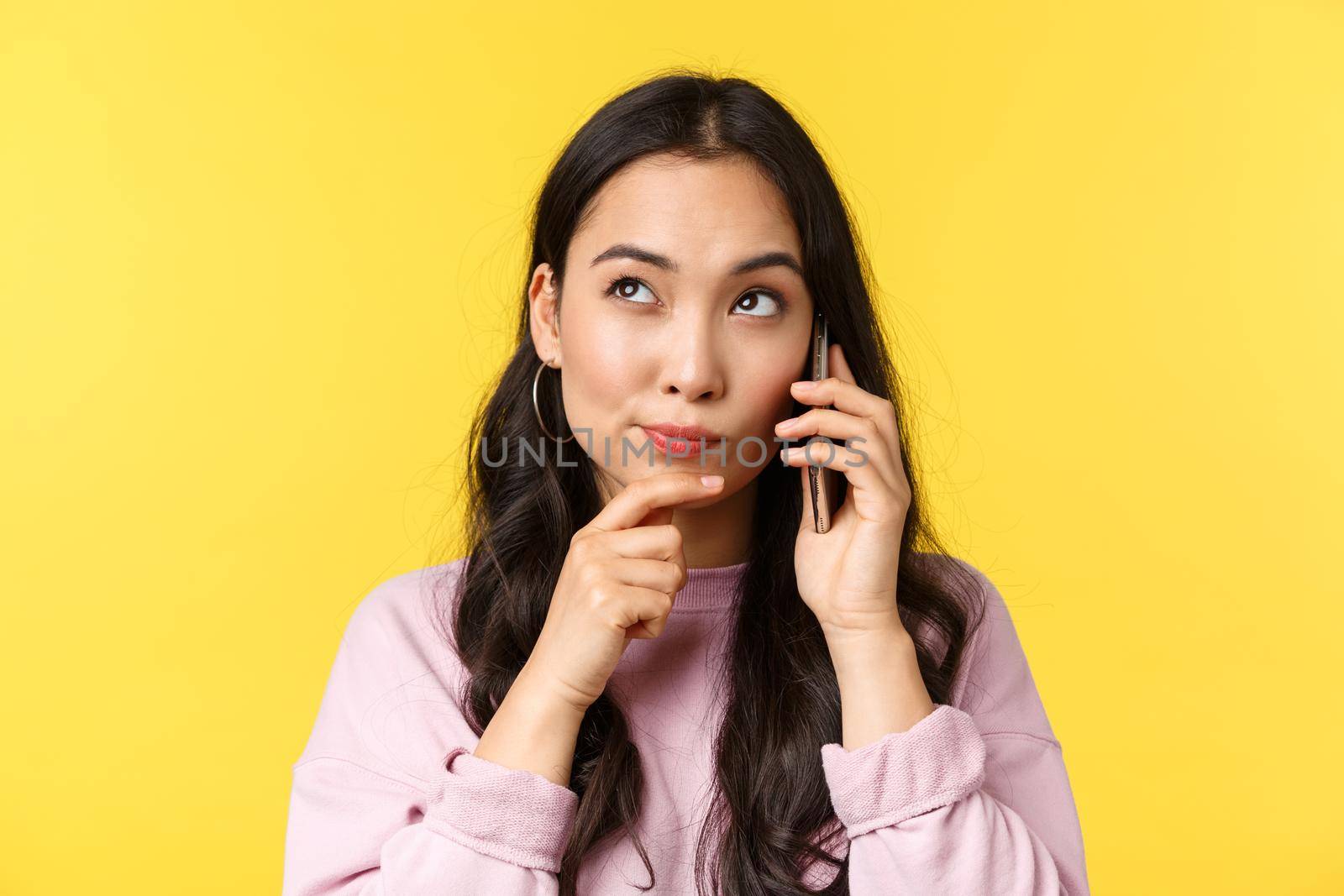 People emotions, lifestyle leisure and beauty concept. Thoughtful cute asian girl thinking while making phone call, book table or order food from takeaway, look upper left corner as making choice.