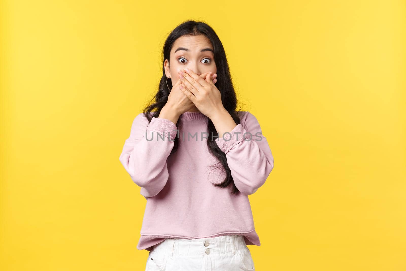People emotions, lifestyle and fashion concept. Shocked and startled asian woman being astonished with big news, press hands to mouth and widen eyes amazed, standing yellow background.