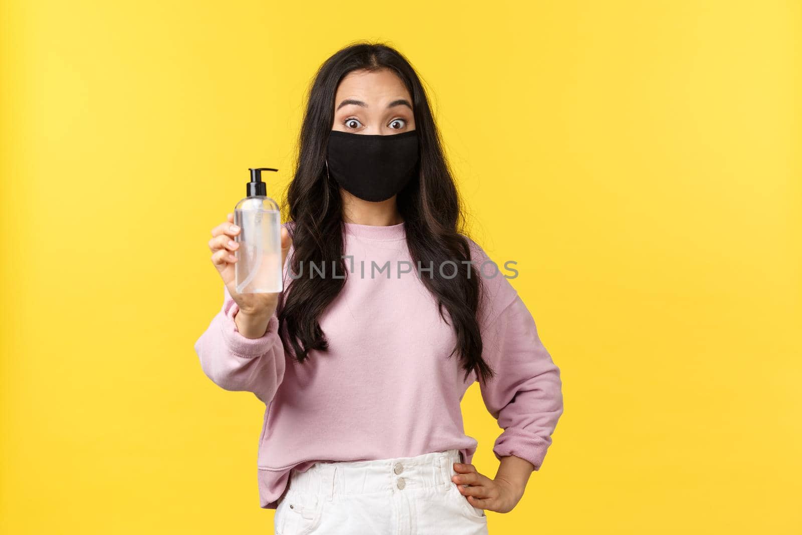 Covid-19, social-distancing lifestyle, prevent virus spread concept. Surprised asian girl in face mask always using hand sanitizer during coronavirus pandemic, recommend hygiene product.