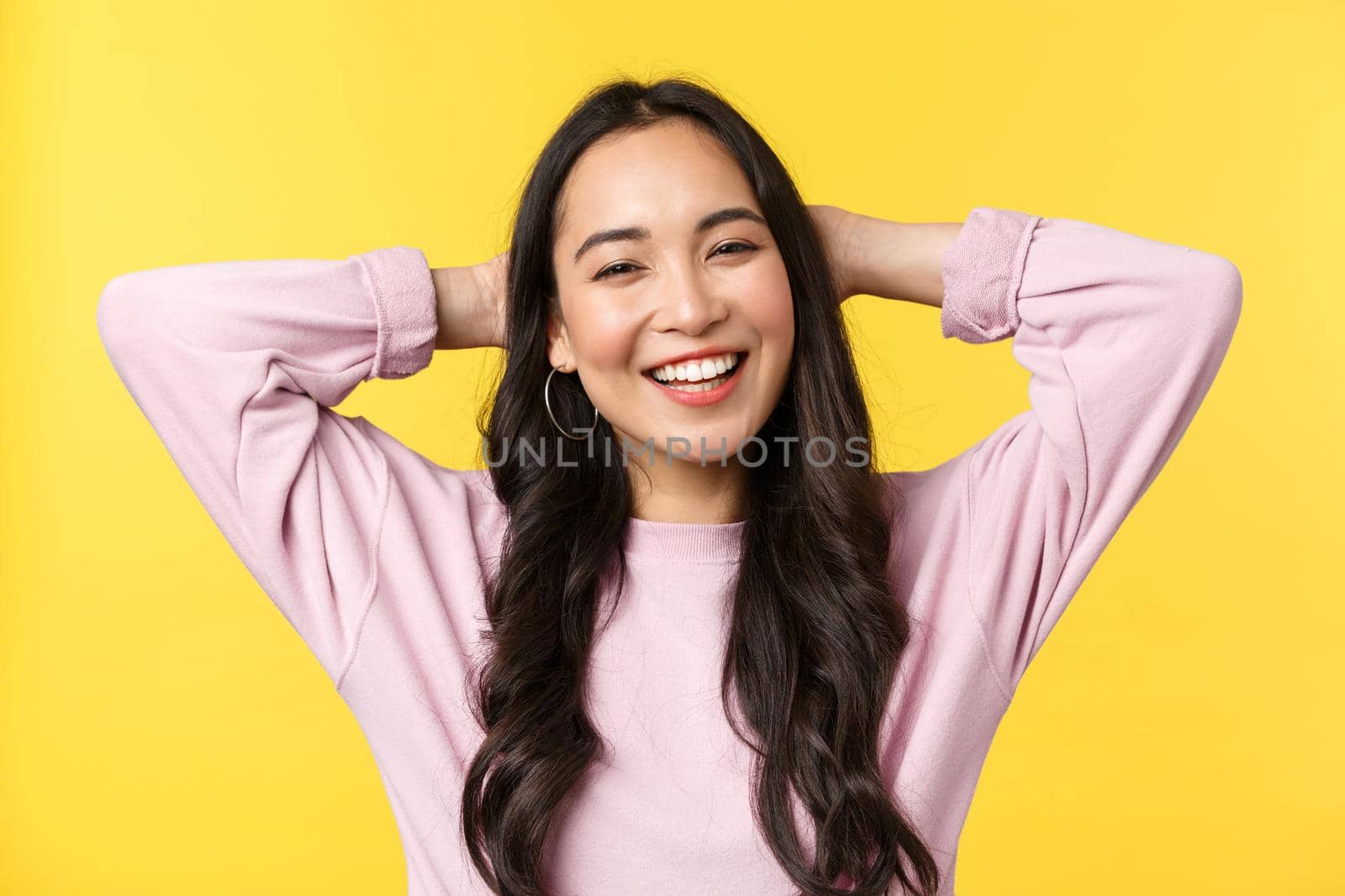 People emotions, lifestyle leisure and beauty concept. Carefree cheerful asian girl smiling broadly, holding hands behind head, enjoying summer weekends, standing yellow background by Benzoix