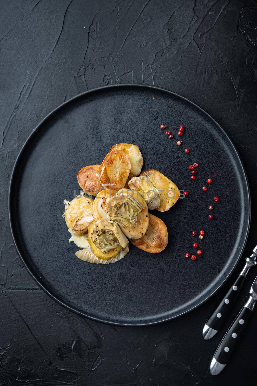 Baked potato, artichoke with fennel al forno, on black textured background, top view
