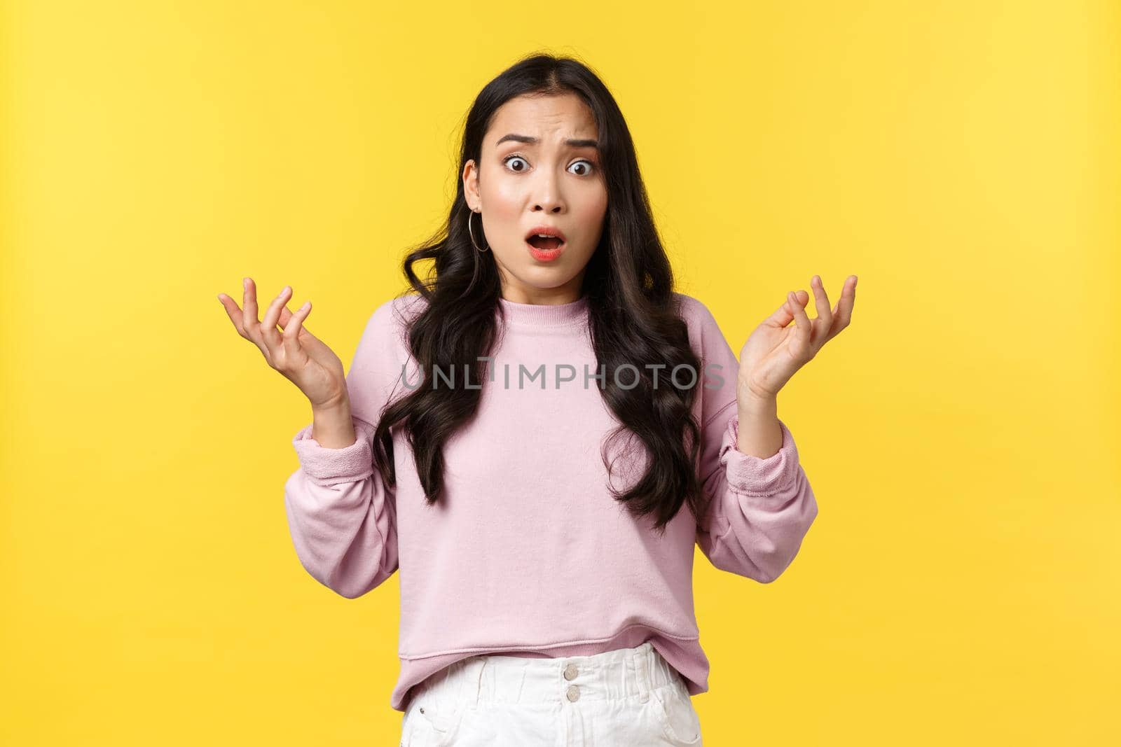 People emotions, lifestyle and fashion concept. Shocked asian woman in panic, looking frustrated and alarmed as hear bad news, raising hands in dismay, got in trouble, yellow background.