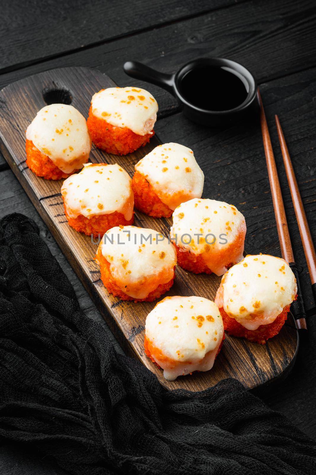 Baked sushi maki rolls with salmon, crab, cucumber, avocado, flying fish roe and spicy sauce, on black wooden table background by Ilianesolenyi
