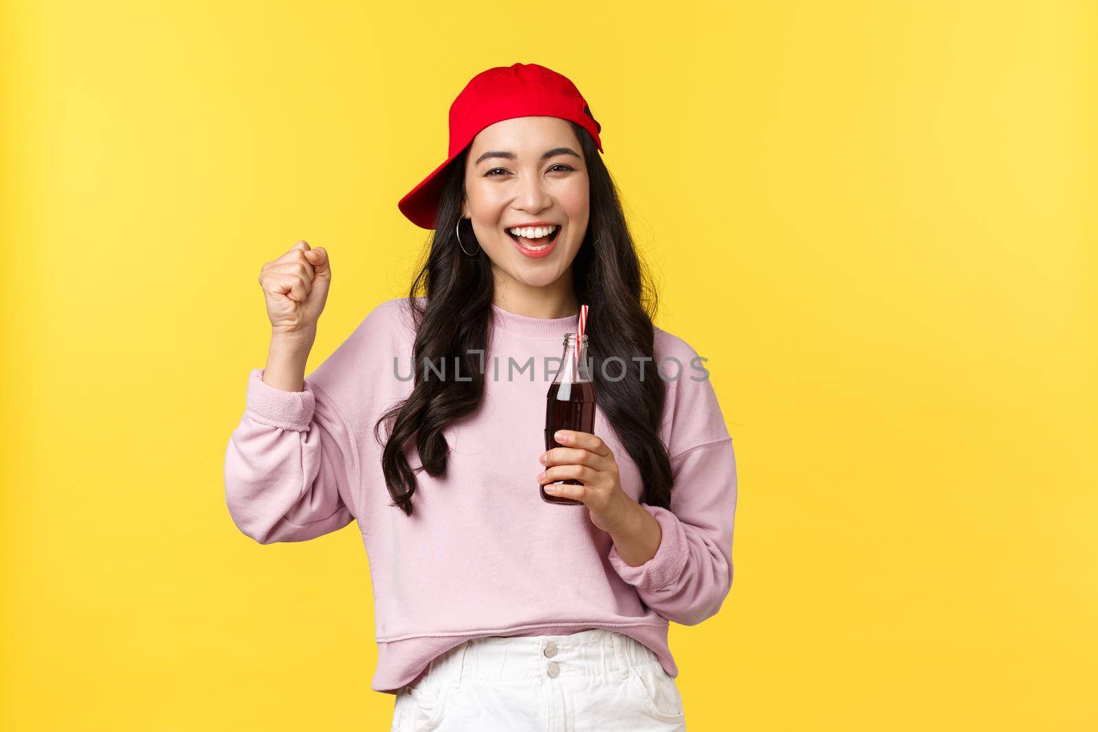 People emotions, drinks and summer leisure concept. Enthusiastic happy asian girl enjoying her soda, drinking beverage and dancing, smiling cheerful, standing yellow background.