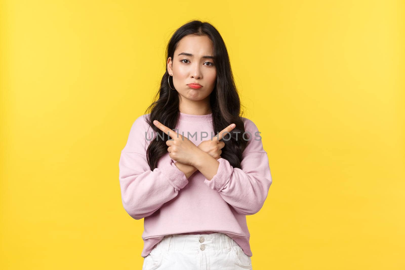 People emotions, lifestyle and fashion concept. Indecisive sad woman troubled making choice, pouting upset and pointing sideways at left and right variants, standing yellow background.