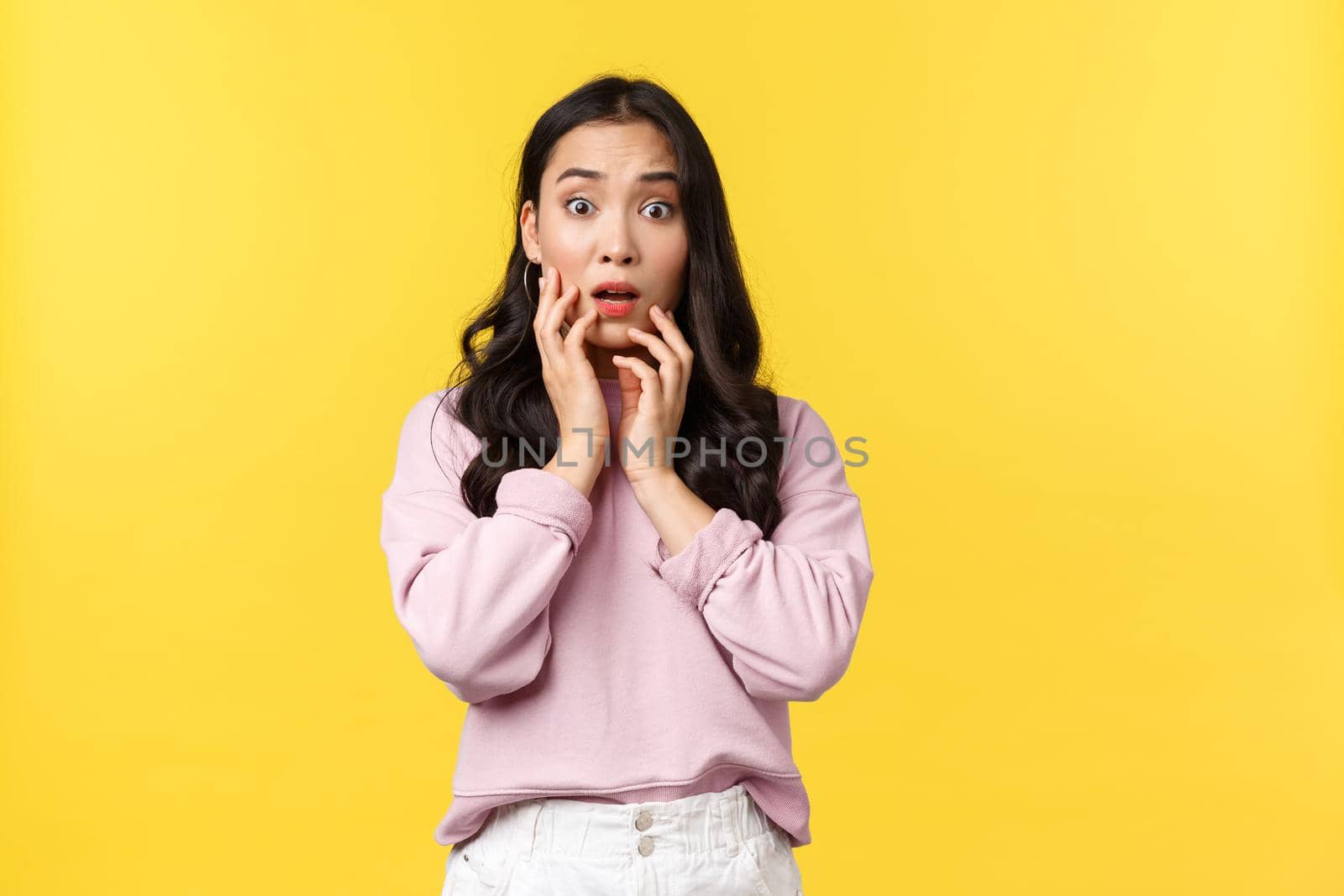People emotions, lifestyle and fashion concept. Shocked and concerned insecure asian woman react to bad shocking news, gasping and touching face, stare anxious at camera, yellow background.