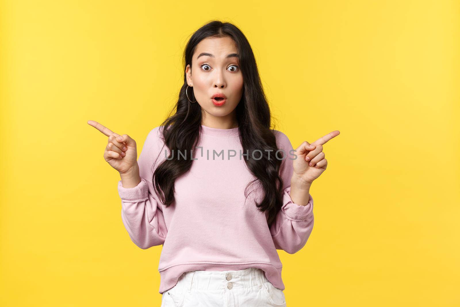 People emotions, lifestyle and fashion concept. Enthusiastic good-looking asian stylish woman say wow and look surprised as pointing fingers sideways, showing left and right, yellow background by Benzoix