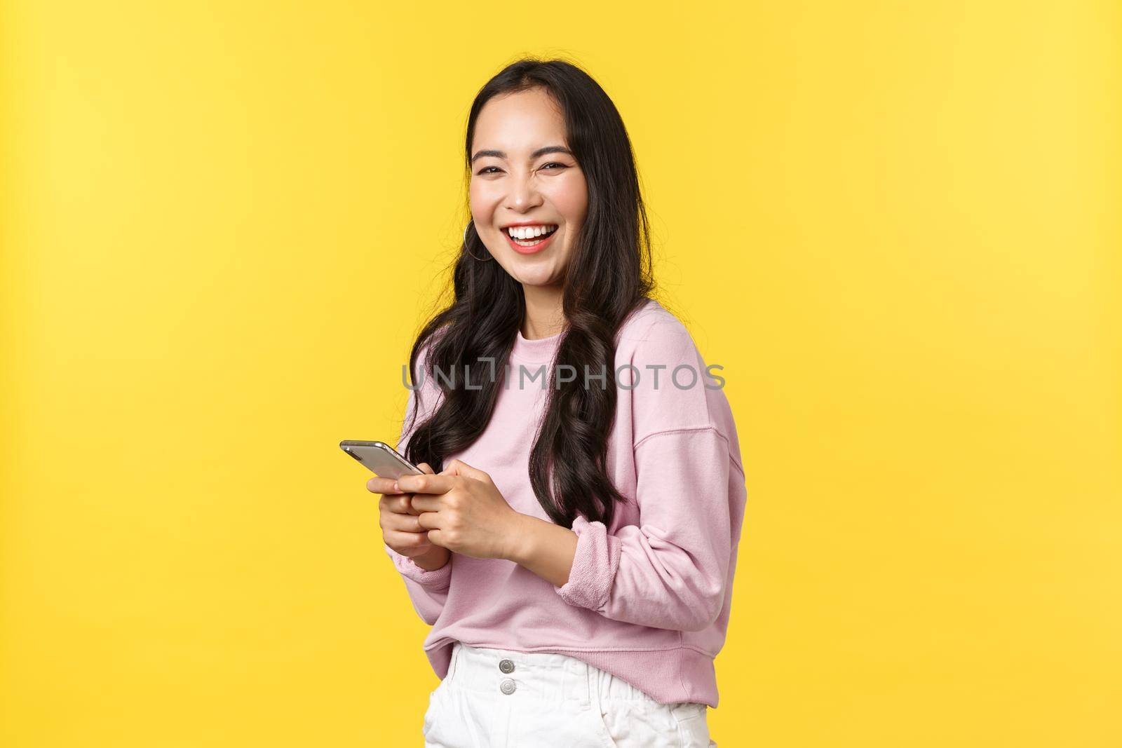 People emotions, lifestyle leisure and beauty concept. Cheerful smiling happy asian woman, turn at camera and laughing after reading funny post on social media app, holding smartphone.