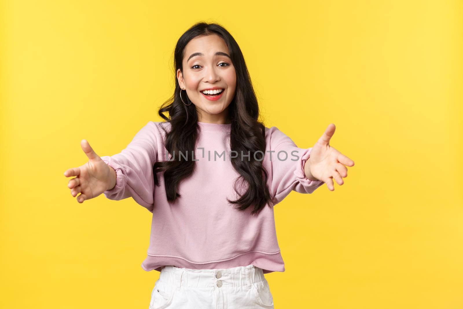People emotions, lifestyle and fashion concept. Lovely korean girl extend hands and reaching camera to give supportive hug, cuddle or embrace friend, congratulating or praising, yellow background.