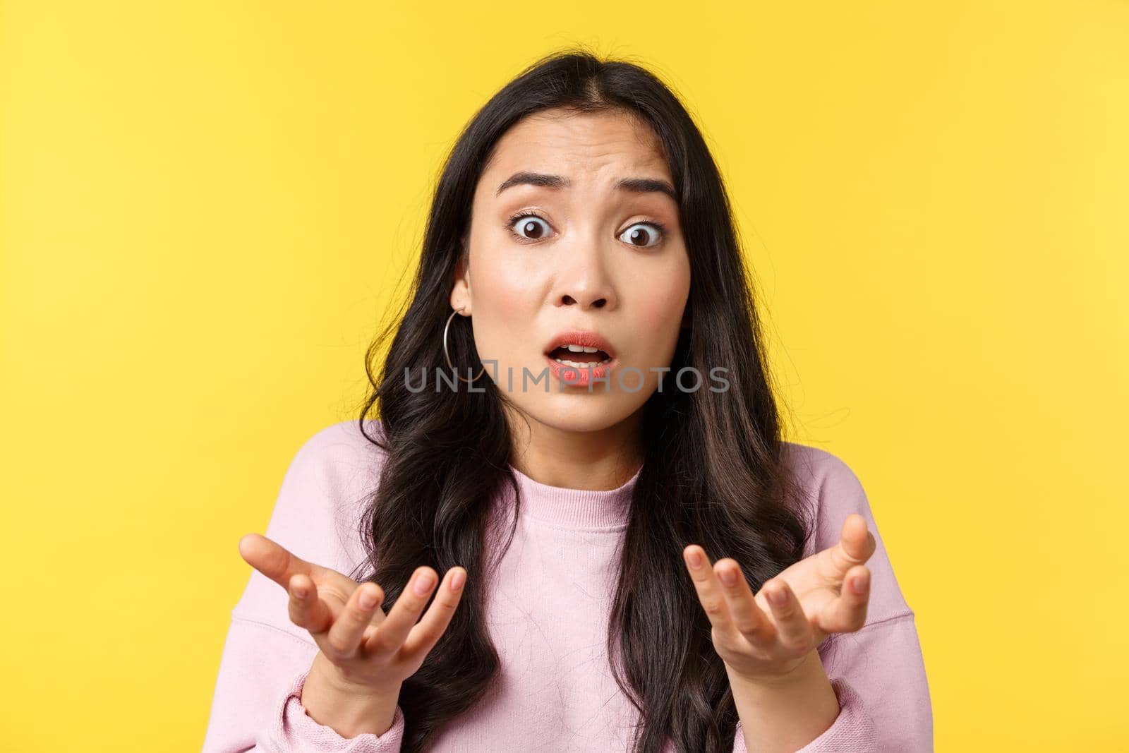 People emotions, lifestyle leisure and beauty concept. Close-up of anxious and confused asian girl cant understand what wrong, shrugging, asking question with worried face, yellow background.