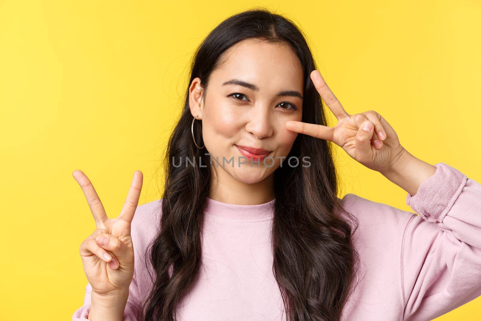 People emotions, lifestyle leisure and beauty concept. Kawaii pretty japanese girl showing peace signs and smiling cute, standing over yellow background advertising product.